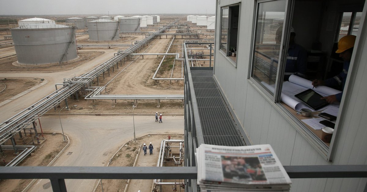 Manos de técnicos analizando planos y documentos en un entorno industrial, con el fondo difuminado de una refinería de petróleo.